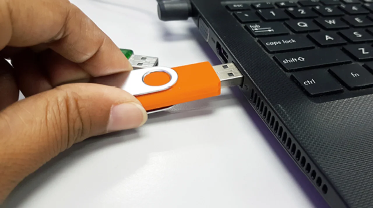 Hand inserts a USB stick into the side of a laptop