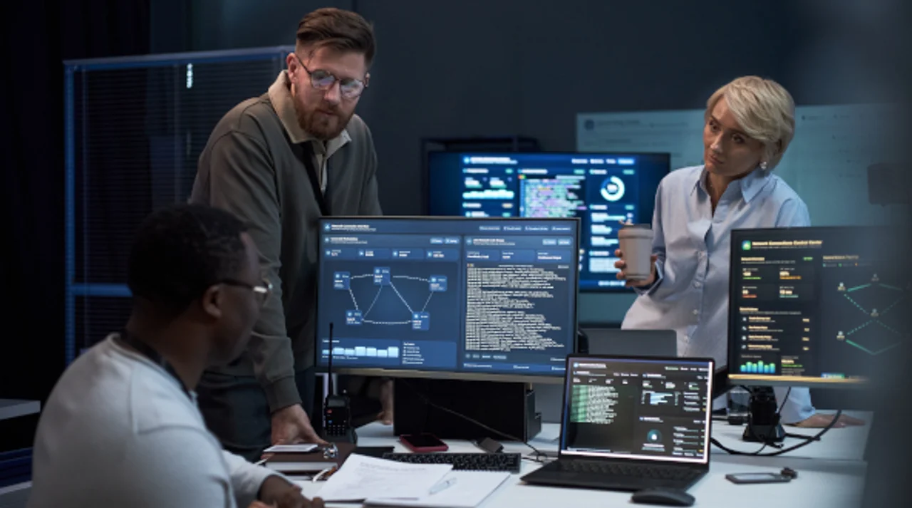 IT team analyzing digital monitoring dashboards and source code on multiple screens