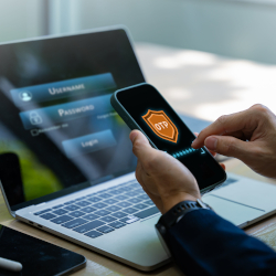 Person nutzt ein Smartphone zur Zwei-Faktor-Authentifizierung am Laptop