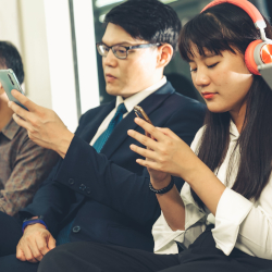 Zwei Pendler nutzen Smartphones, während eine Person Kopfhörer trägt