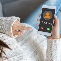 Eine Frau auf einem Sofa h&auml;lt ein Smartphone in der Hand, auf dem ein Anruf einer unbekannten Nummer eingeht